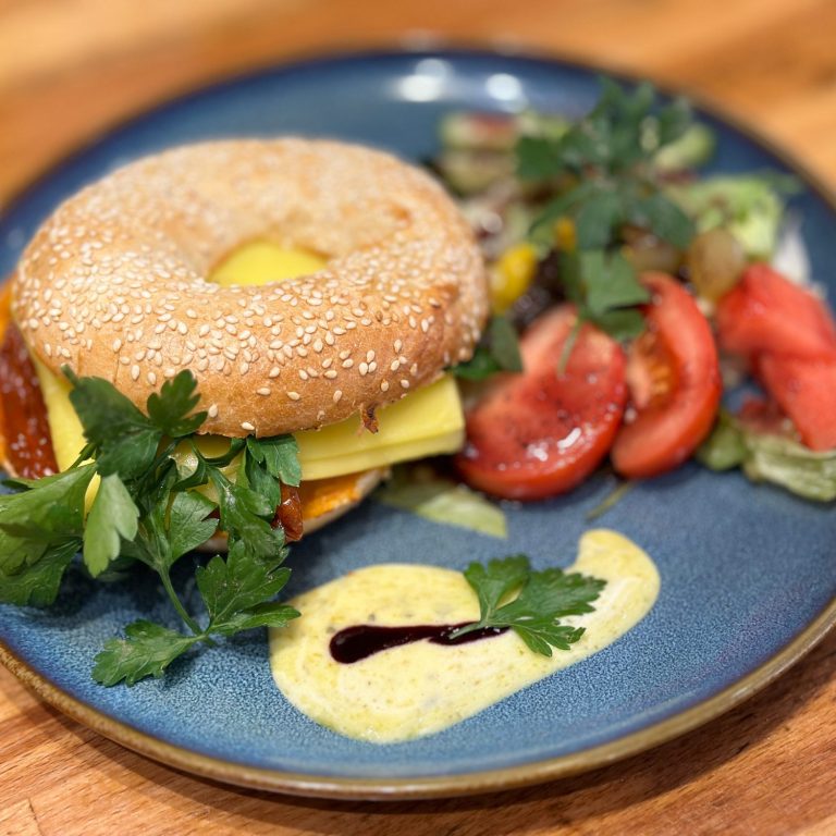 bagel Bagel mit Käse, Salat, Tomaten und Soße auf einem blauen Teller.