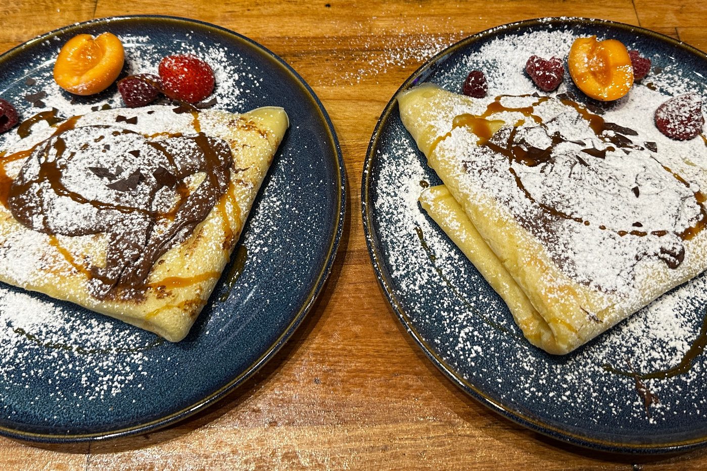 Zwei gefüllte Crepes auf Tellern, garniert mit Früchten und Puderzucker.